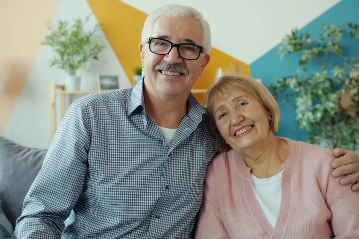Un couple souriant, assis côte à côte sur le canapé de leur salon
